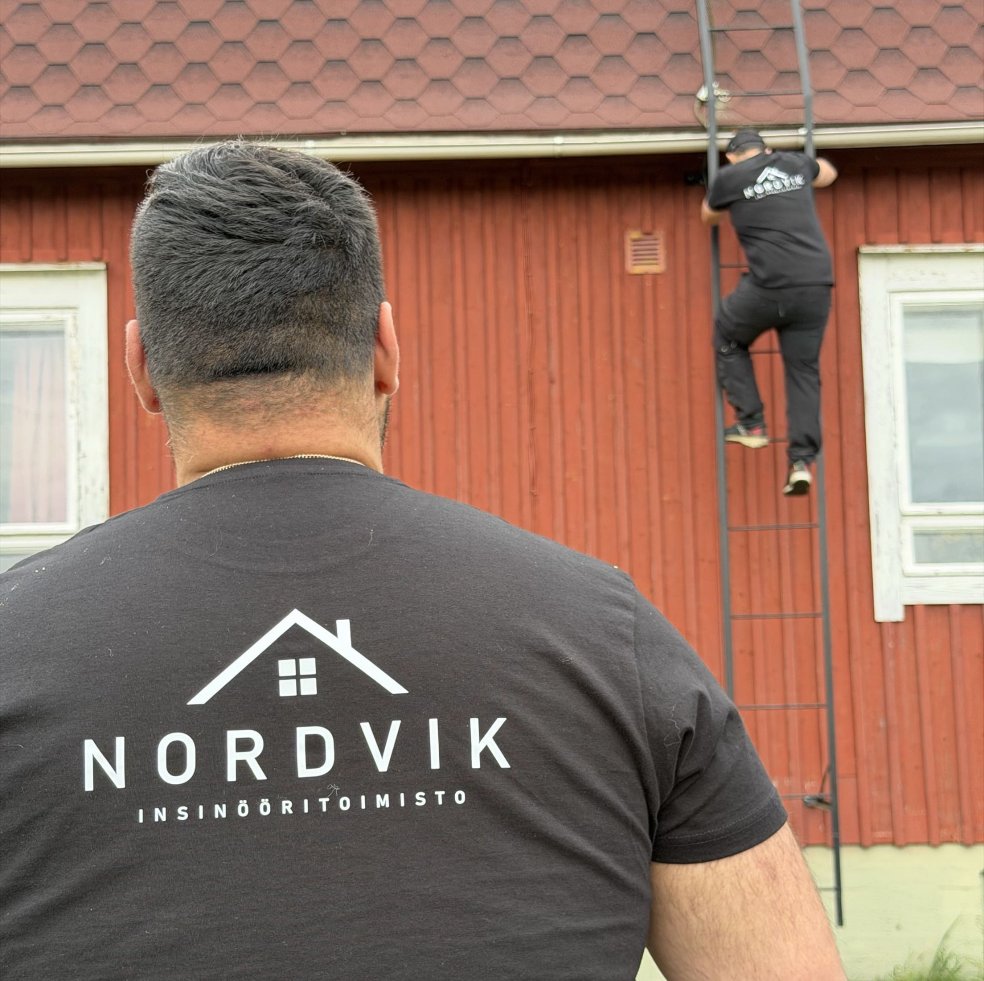 Nordvikin kuntotarkastaja tikkailla punaisen puutalon ulkoseinällä Uudellamaalla