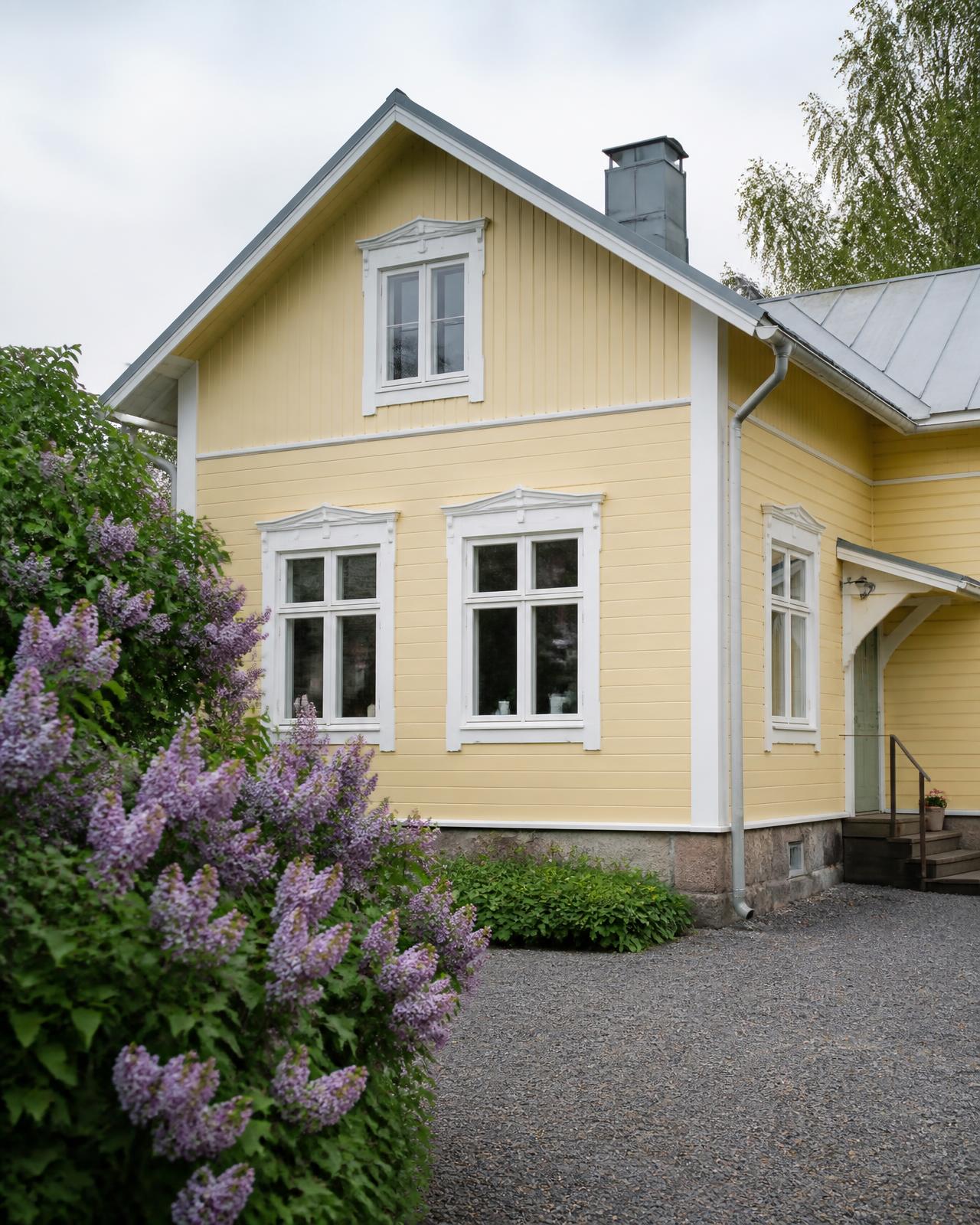 Vanha vaaleankeltainen suomalainen puutalo valkoisin ikkunanpuittein ja syreenipensas pihalla